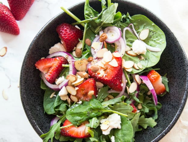 Photo of a Strawberry Spinach Salad in a Black bowl on a Kitchen counter